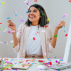 A woman joyfully celebrates at her desk, surrounded by confetti, commemorating work anniversaries with personalized chocolate gifts