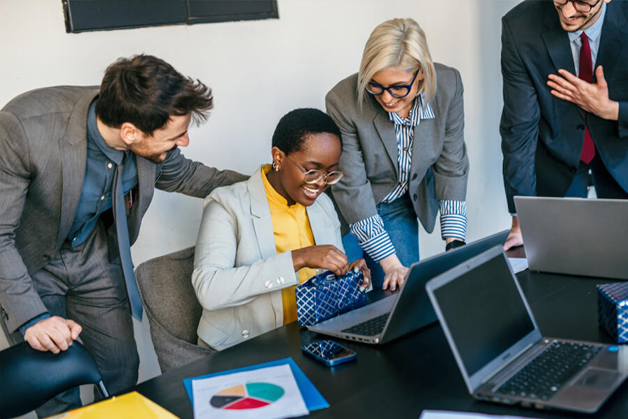 A diverse group of business professionals collaborating on a laptop, surrounded by employee chocolate gifts on the table