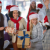 A cheerful group wearing Santa hats joyfully holds colorful presents, embodying the spirit of festive corporate gifting