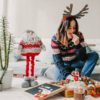 A woman wearing a Santa hat sits on a couch beside a beautifully decorated Christmas tree, embodying holiday cheer