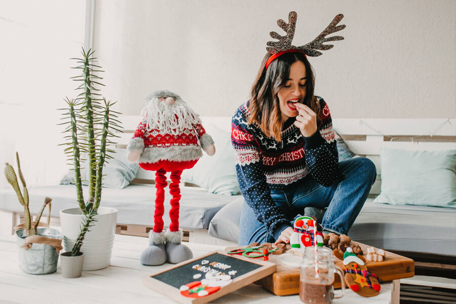 A woman wearing a Santa hat sits on a couch beside a beautifully decorated Christmas tree, embodying holiday cheer