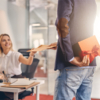 A man presents a gift to a woman in an office setting, showcasing a moment of appreciation and celebration