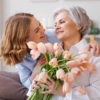 A woman embraces an older woman, presenting her with a bouquet of flowers in celebration of Mother's Day