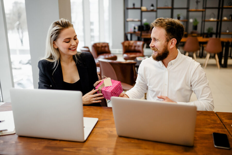 A man and woman at a table with laptops, celebrating Administrative Professionals Day with chocolate gifts