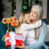 Grandmother and granddaughter sitting on a sofa, joyfully holding a bouquet of flowers for Grandparents Day