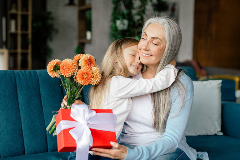 Grandmother and granddaughter sitting on a sofa, joyfully holding a bouquet of flowers for Grandparents Day