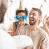 A man joyfully laughs while holding a birthday cake topped with a candle, celebrating a special occasion