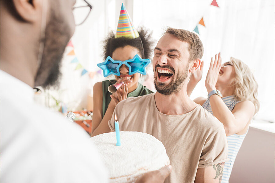 A man joyfully laughs while holding a birthday cake topped with a candle, celebrating a special occasion